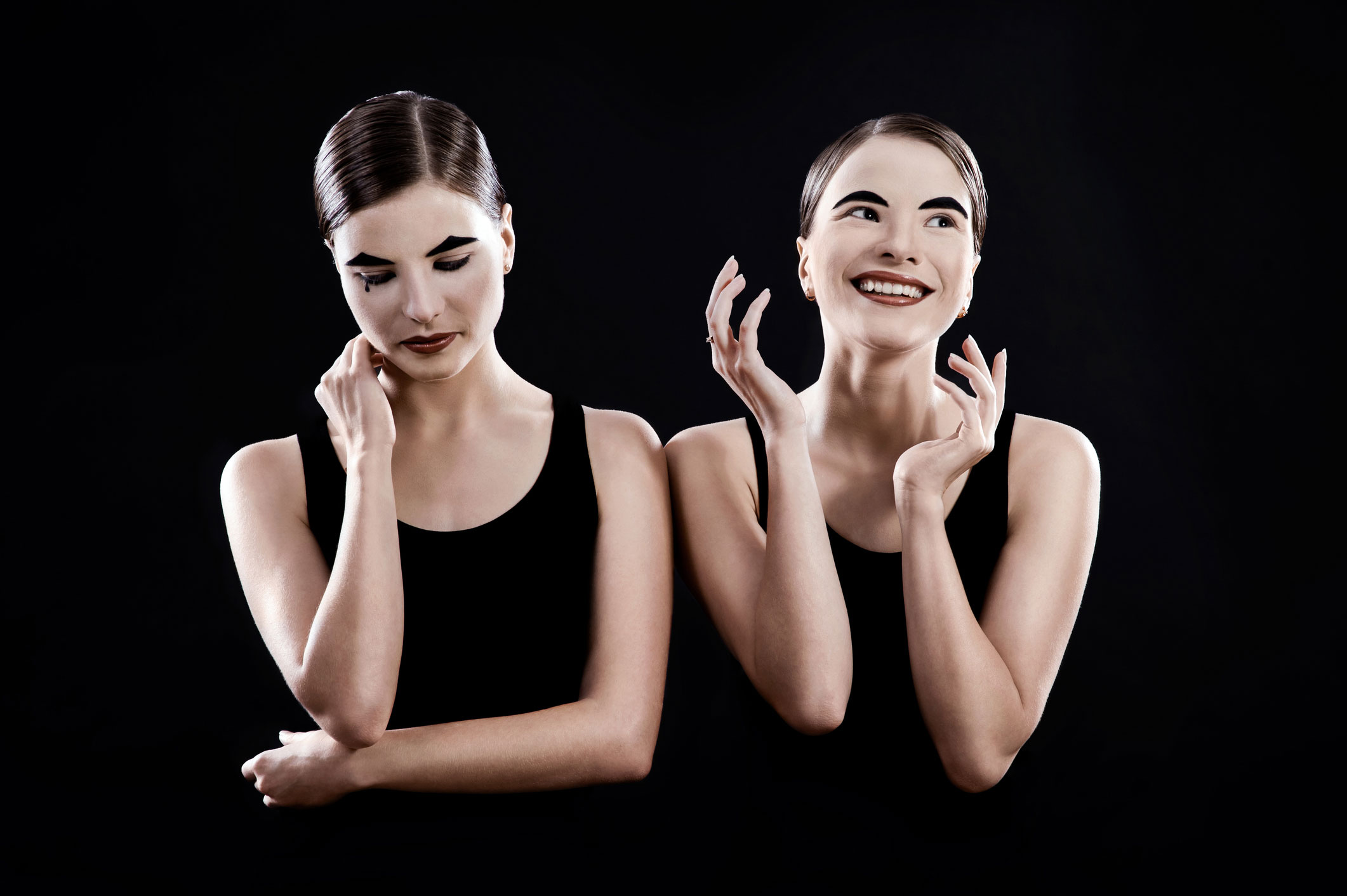 Duas mulheres mimicas, representando suas emoções. A primeira representa a tristeza e a segunda a alegria.